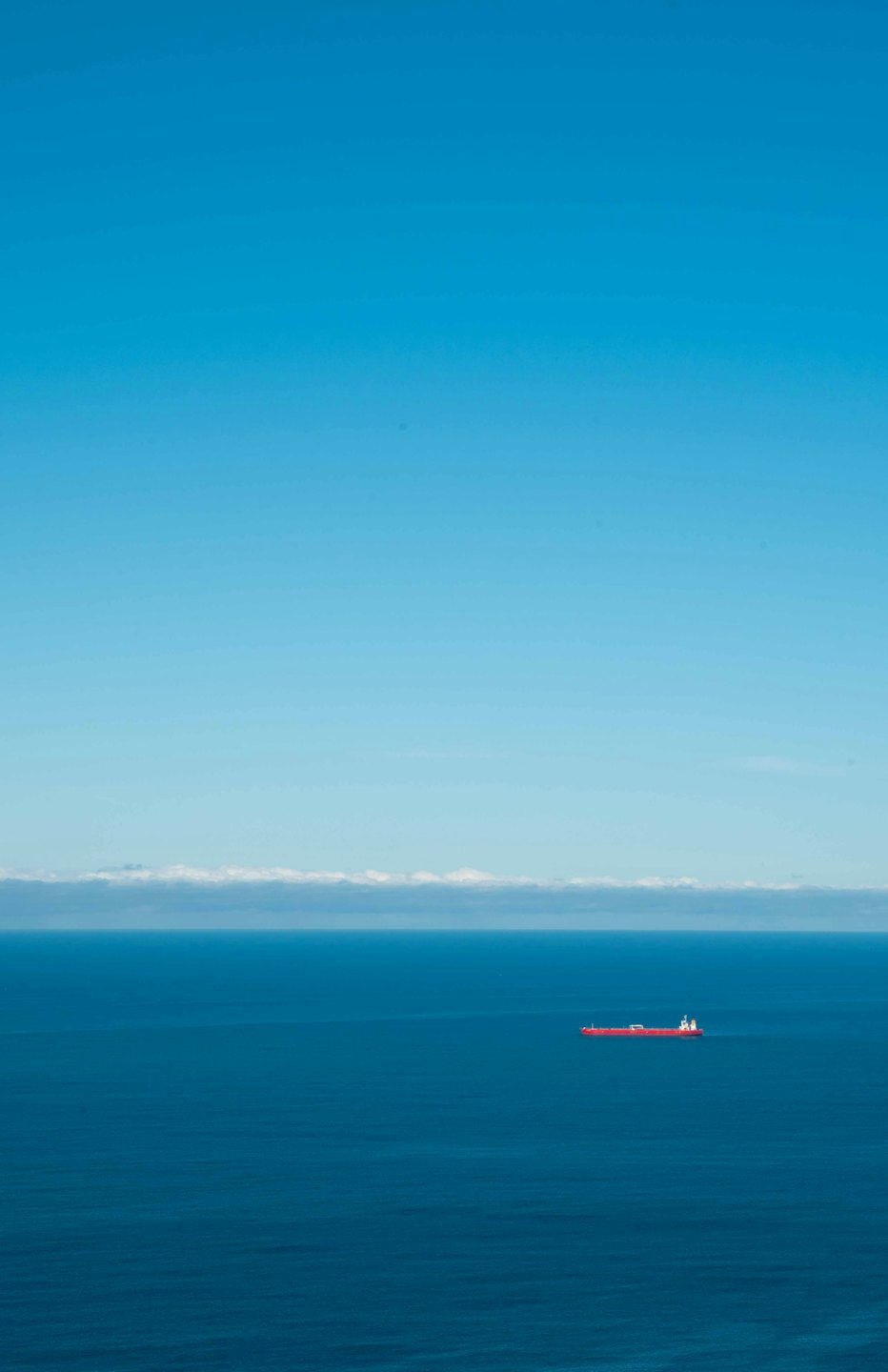 A small red cargo ship sails across the calm ocean.